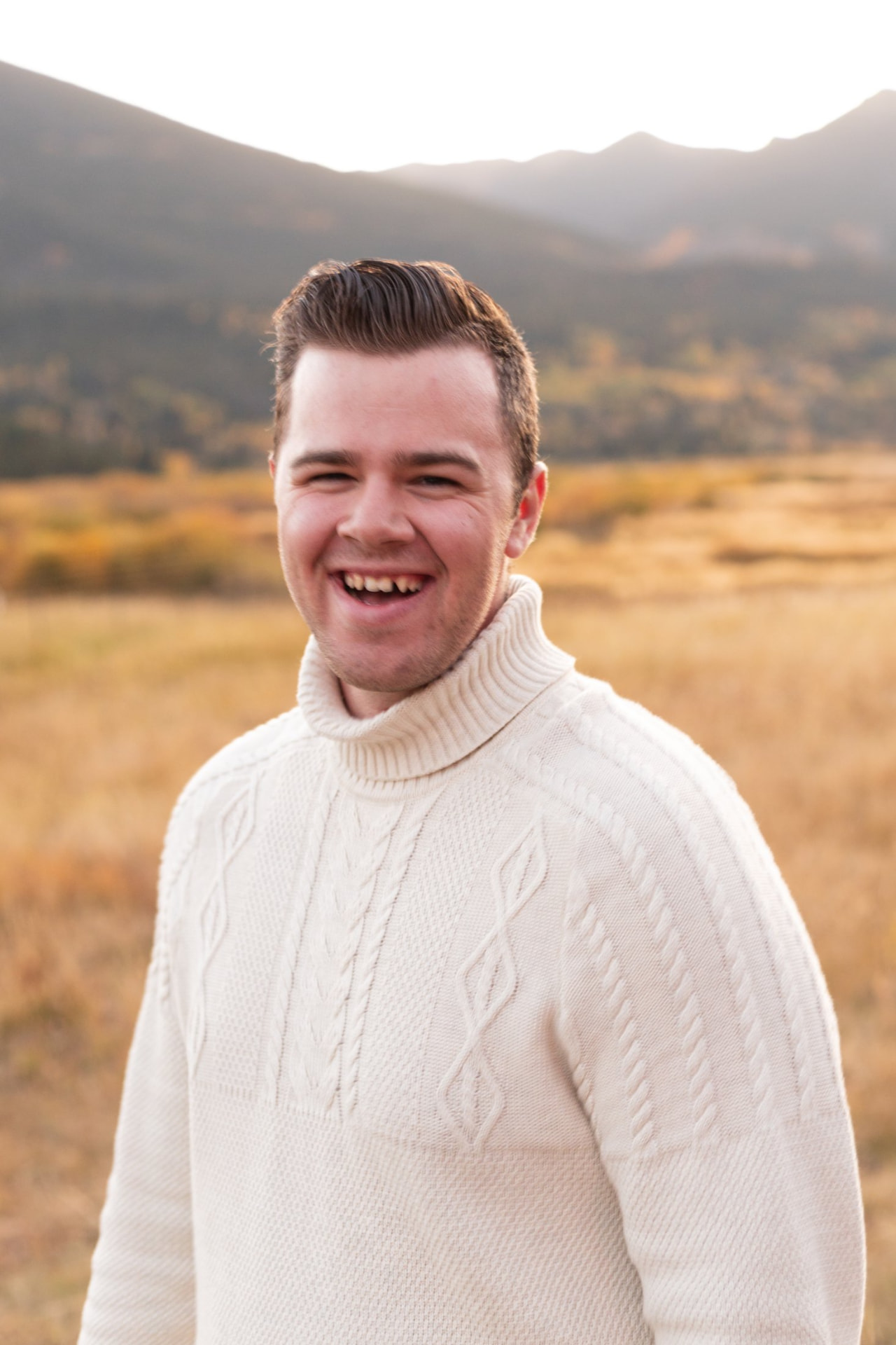 Abel Scott laughing in a cream sweater in a golden Colorado field at sunset